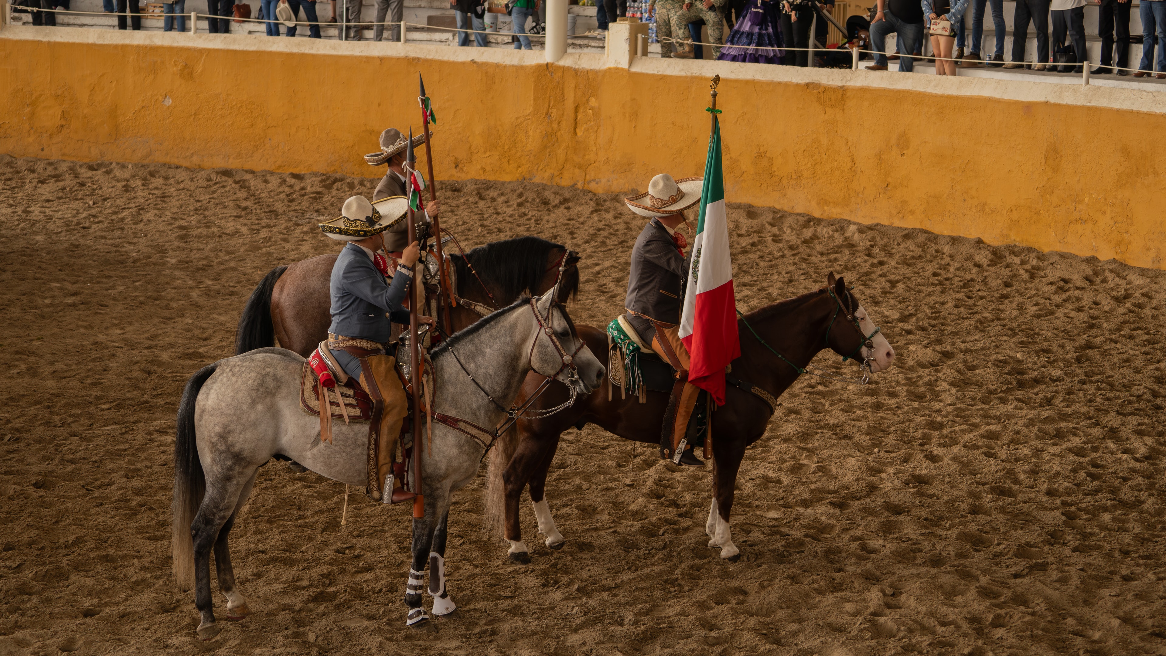 Charros a caballo portando la bandera mexicana en el Lienzo Charro de Jalisco
