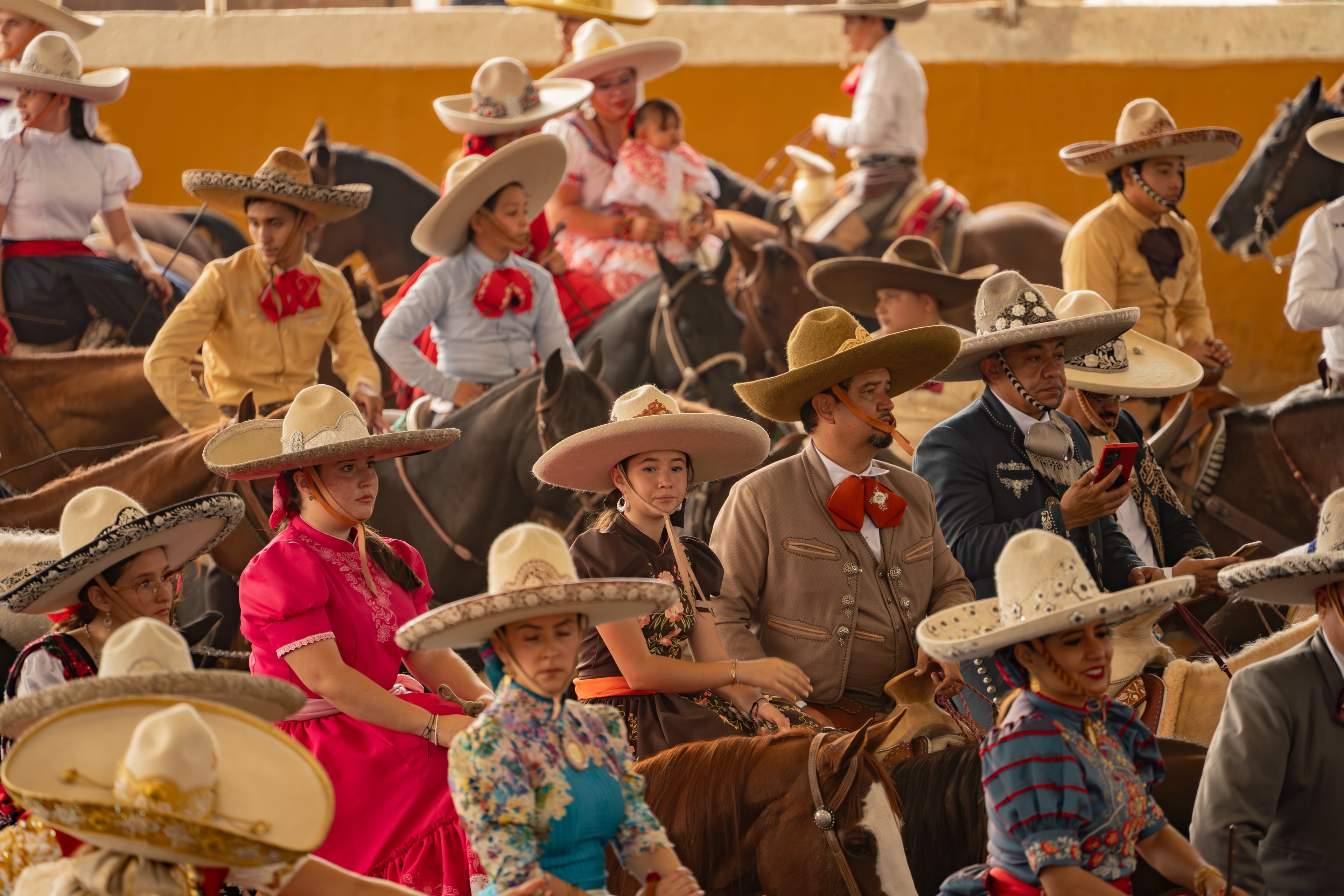 Gran grupo de charros y escaramuzas a caballo en el Lienzo Charro de pared amarilla