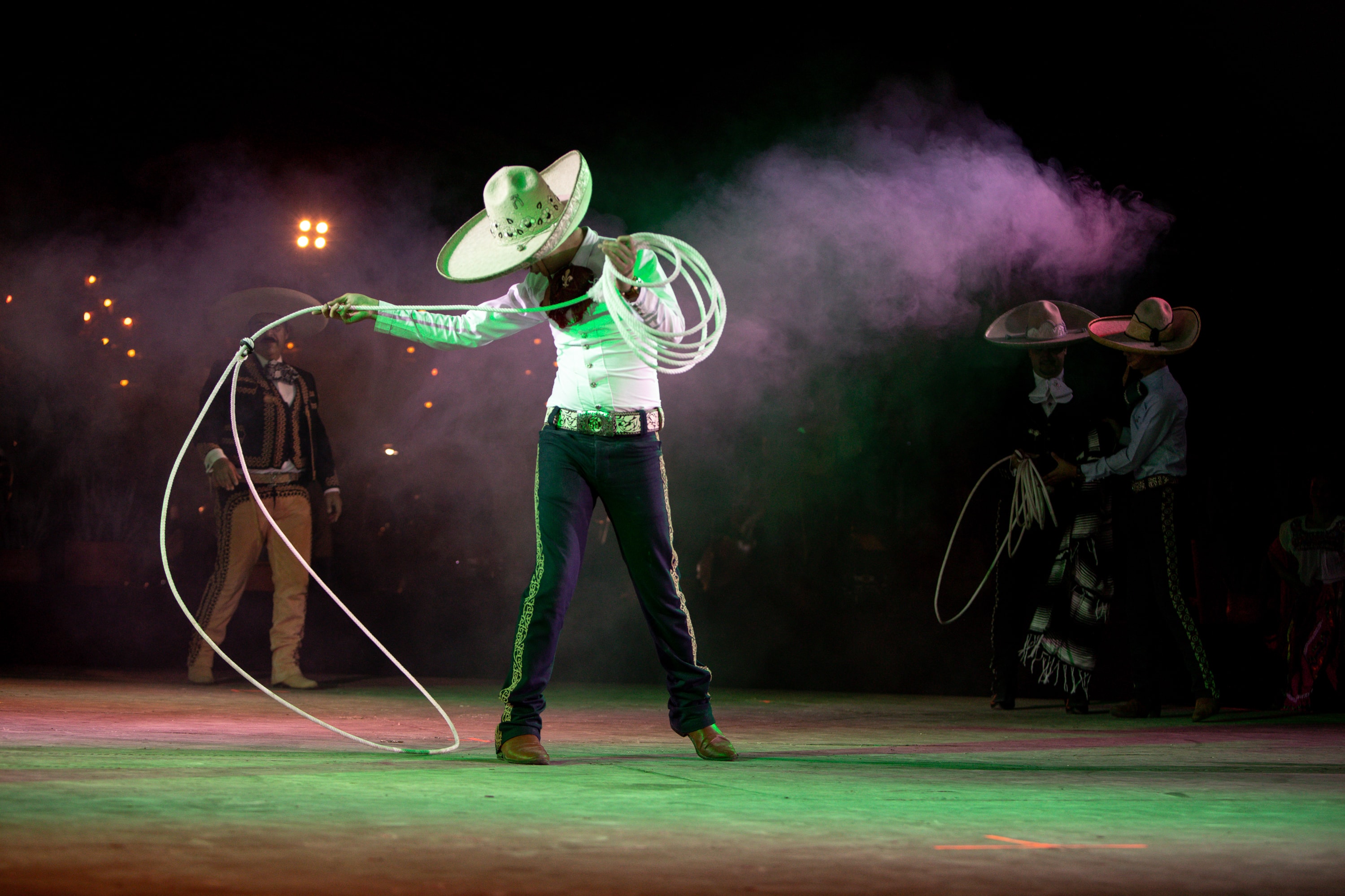 Charro con reata luminosa entre humo verde en espectáculo nocturno