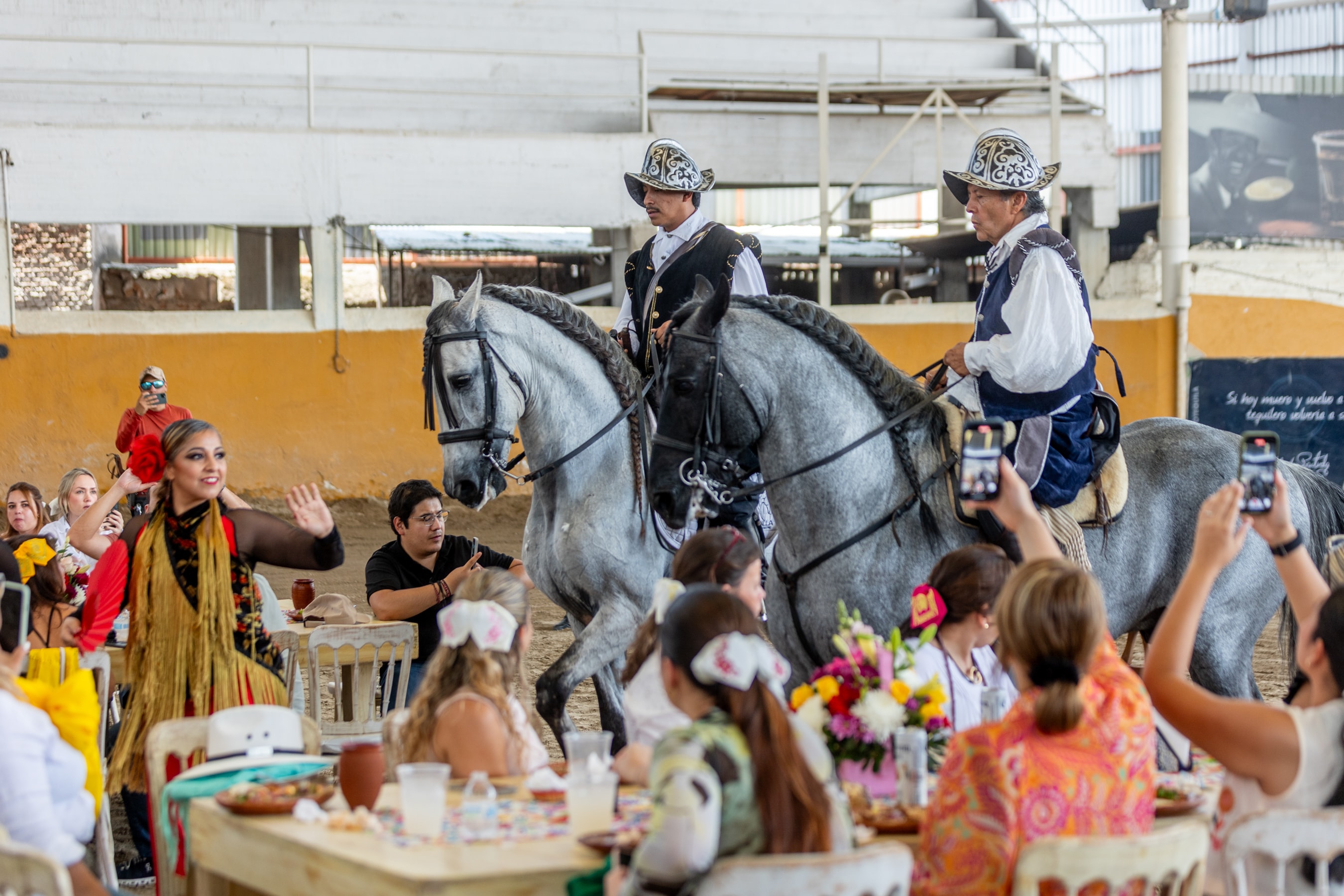 Charros a caballo tordillo con bailarina folklórica y grupo de invitados en el Lienzo